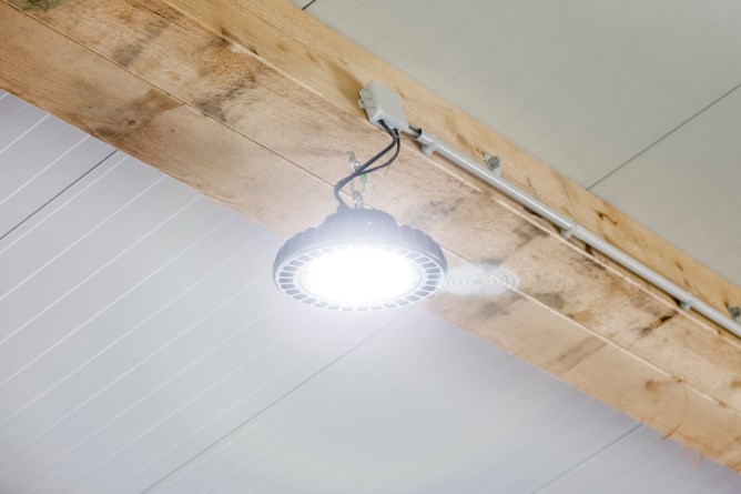 Der eingeschaltete 100 W Kerbl LED Hallenstrahler  an der Decke an einem Holzbalken montiert